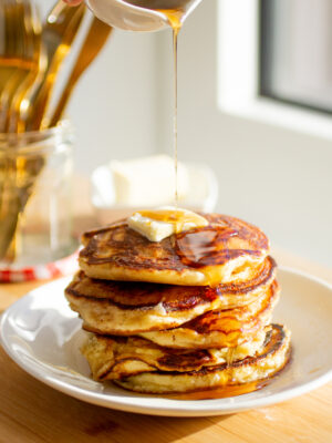 A stack of golden pancakes on a white plate topped with butter and syrup.