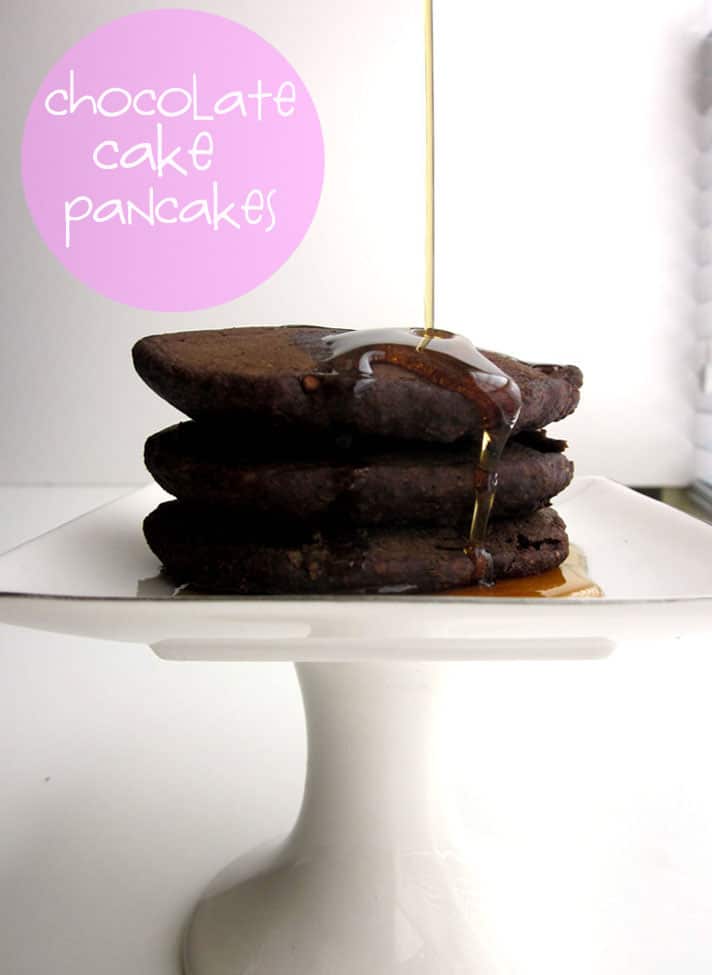 A stack of three chocolate pancakes with maple syrup being poured over.