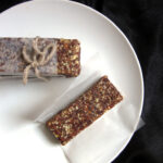 A granola bar on a sheet of parchment paper next to a stack of granola bars on a white plate.