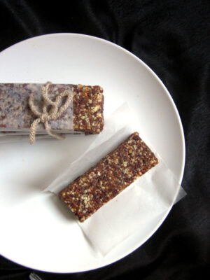A granola bar on a sheet of parchment paper next to a stack of granola bars on a white plate.
