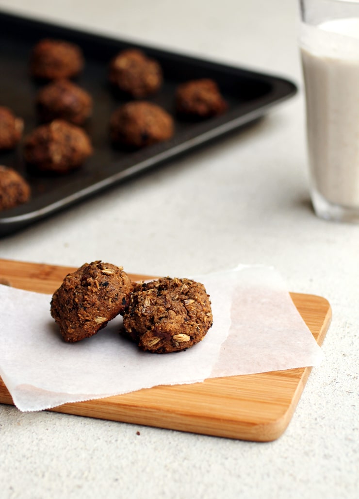 Two grainy cookies on a piece of parchment paper on a cutting board with a baking tray full of cookies in the background.
