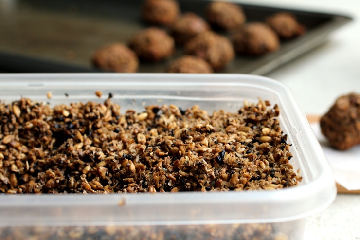 A plastic container full of spent grain with a sheet of baked cookies in the background.