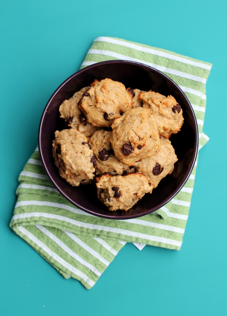 A purple bowl full of banana chocolate chip cookies on top of a green and white striped towel. 