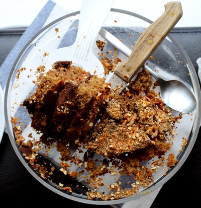 A slice of pretzel cake on a glass cake stand with a knife cutting into it.
