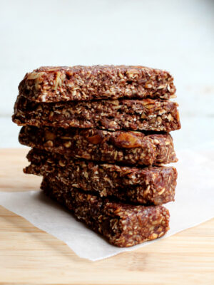 Five date-sweetened granola bars stacked on a sheet of parchment paper on a cutting board.