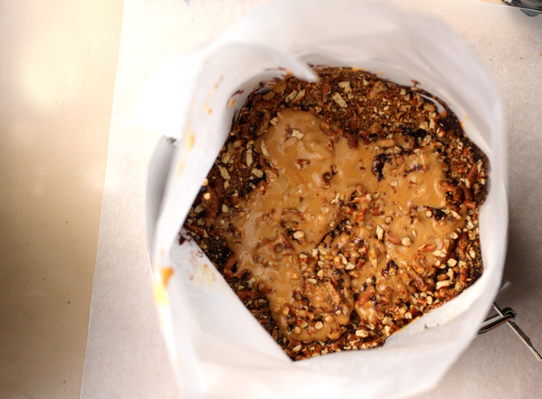 A cake pan lined with parchment paper and filled with a layer of cake, chocolate ganache and burnt honey frosting.