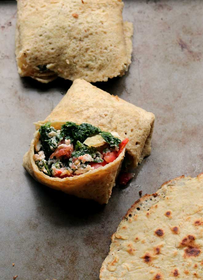 A chickpea flour tortilla on a white plate filled with kale, avocado and carrots.