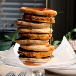 A tall stack of vegan pancakes with a pour of syrup falling over the side.