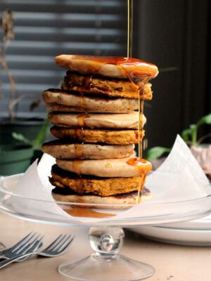 A tall stack of vegan pancakes with a pour of syrup falling over the side.