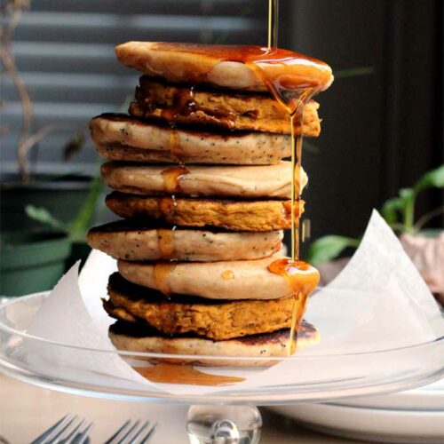 A tall stack of vegan pancakes with a pour of syrup falling over the side.
