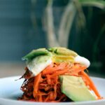 carrot fritters on a white plate with avocado and egg.
