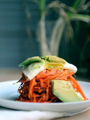 carrot fritters on a white plate with avocado and egg.