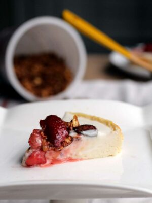 A slice of cheesecake with strawberry compote on a white plate.