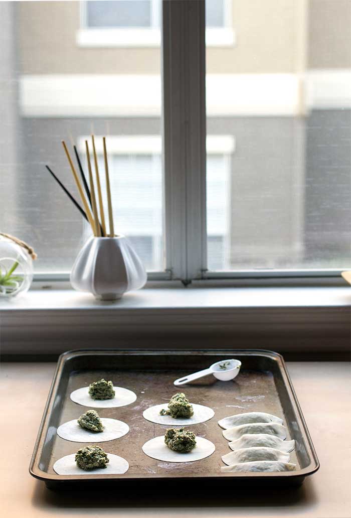 Rounds of dumplings wrappers topped with balls of filling on a baking sheet.