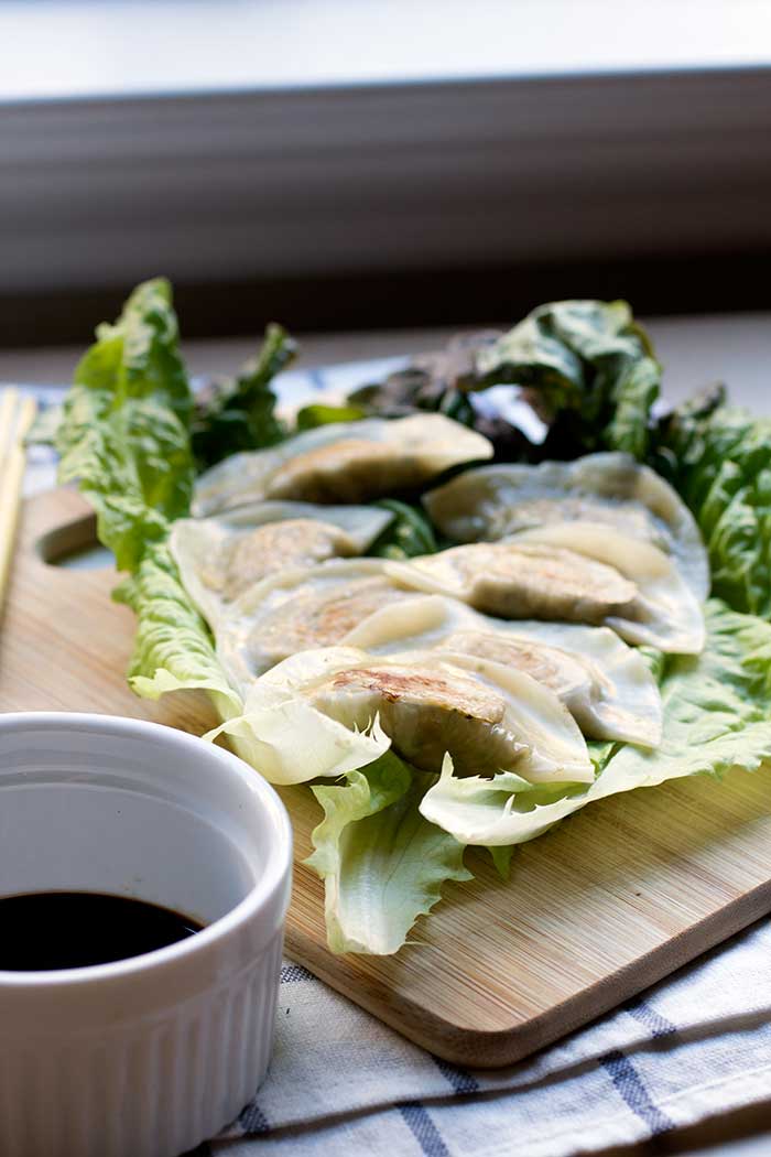 Tofu kale potstickers on top of a large piece of lettuce on a cutting board.