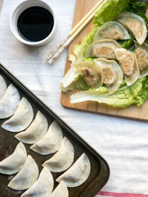 Tofu kale potstickers on top of a large piece of lettuce on a cutting board next to a bowl of soy sauce.