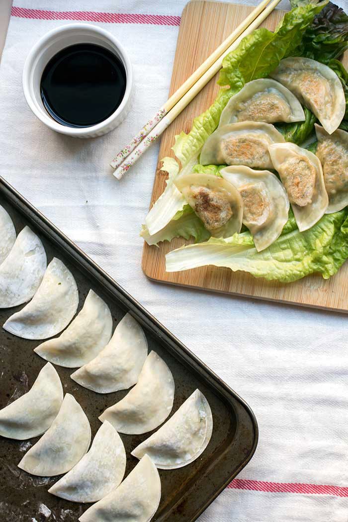 Tofu kale potstickers on top of a large piece of lettuce on a cutting board next to a bowl of soy sauce.
