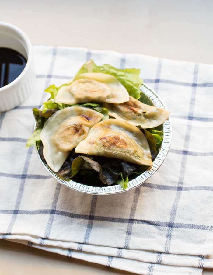 4 tofu kale potstickers on top of lettuce in a silver bowl.