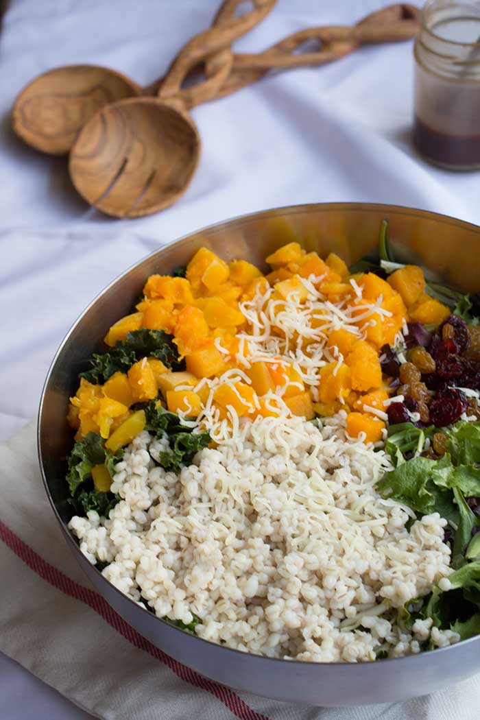 A silver bowl filled with mixed greens, cooked grains and butternut squash.