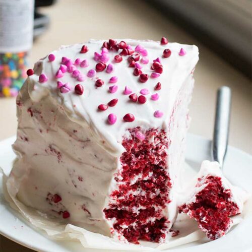 A frosted slice of red velvet cake with a bite taken out of the tip.