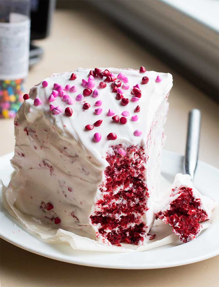 A frosted slice of red velvet cake with a bite taken out of the tip.