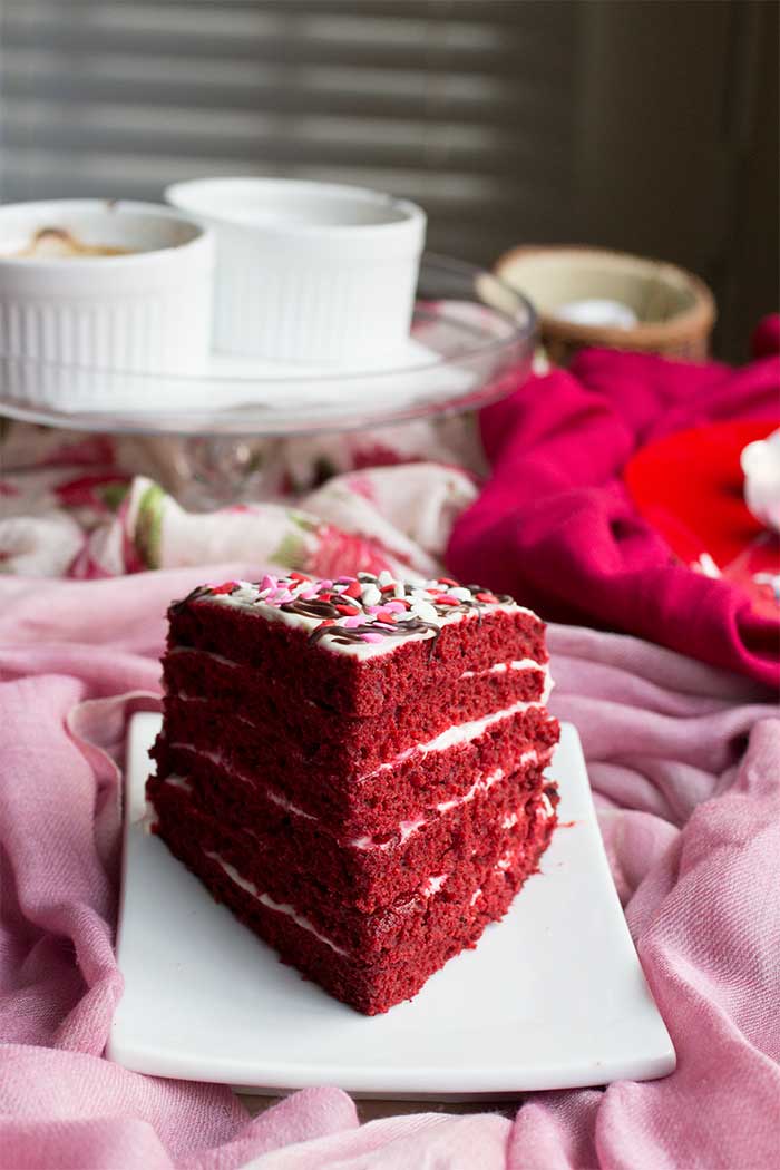 A slice of red velvet cake on a white plate with sprinkles on top.