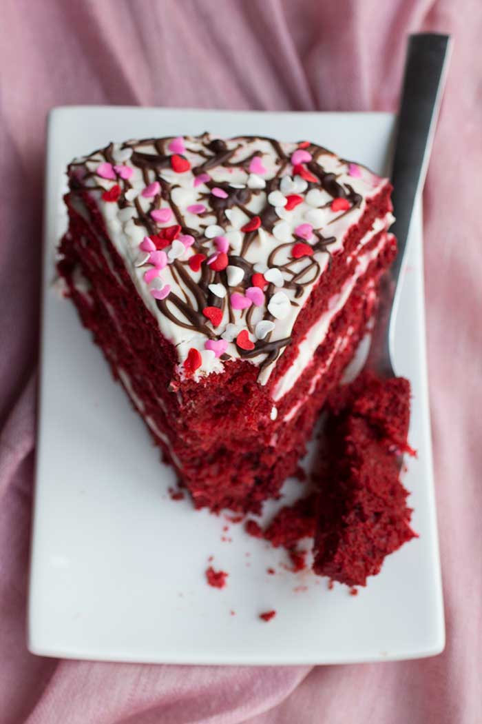 A frosted slice of red velvet cake with a bite taken out of the tip.