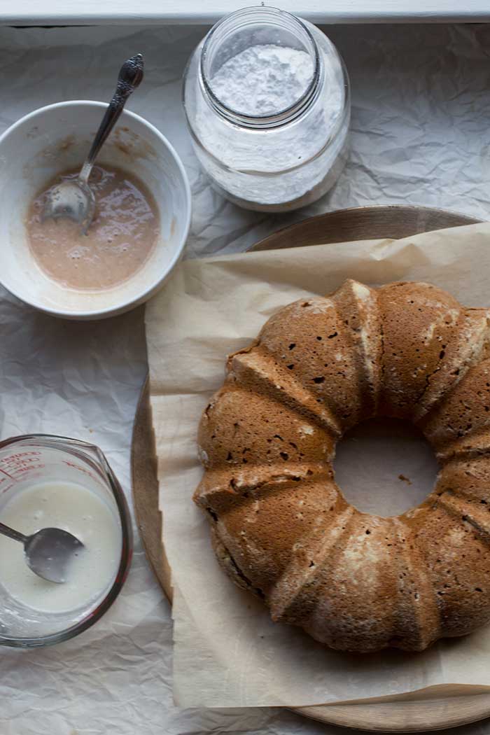 An unfrosted apple bundt cake on a platter next to a bowl of cinnamon icing.