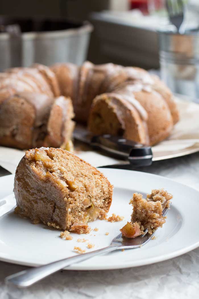 A slice of apple bundt cake on a white plate with a bundt cake in the background.