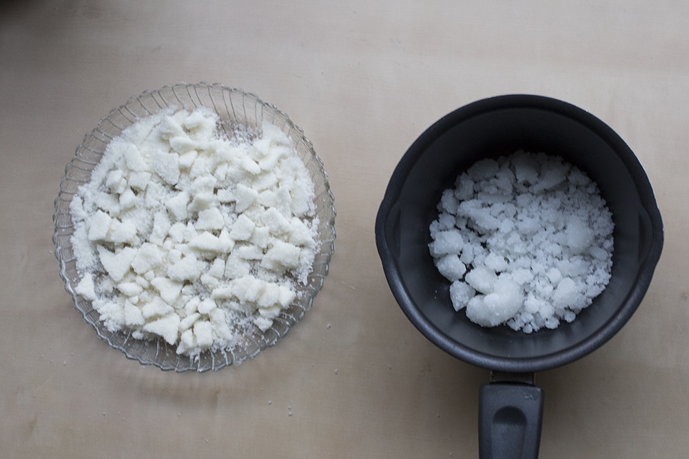 A glass plate full of shattered sugar next to a black saucepan full of crystallized pearl sugar.