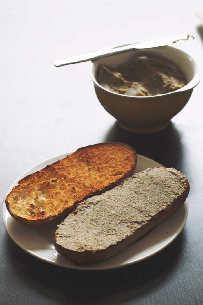 Two halves of a toasted bread roll on a white plate with lentil pate spread on one bread half.