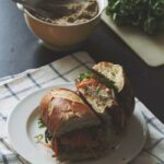 A banh mi cut in half on a white plate to show the shredded veggies and tofu in the middle.