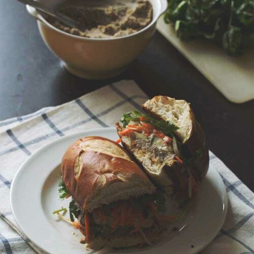 A banh mi cut in half on a white plate to show the shredded veggies and tofu in the middle.