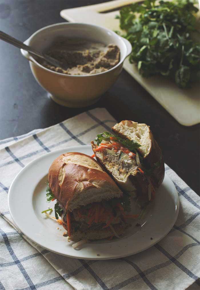 A banh mi cut in half on a white plate to show the shredded veggies and tofu in the middle.