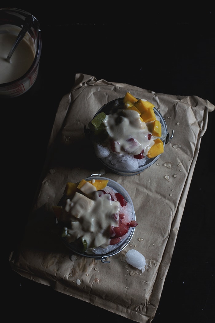 Two silver mini pails filled with shaved ice, chopped mango and strawberries and topped with condensed milk.