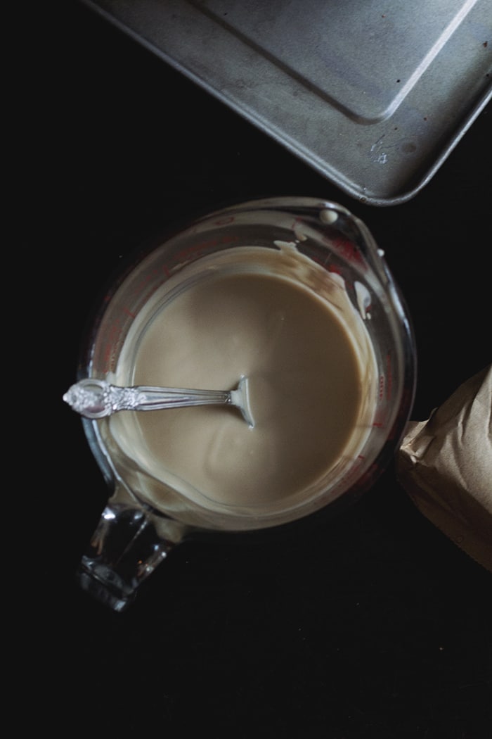 A glass measuring cup full of condensed milk with a spoon submerged inside.