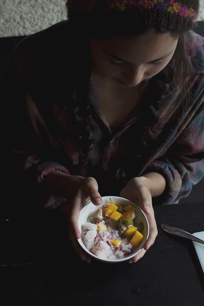 A girl holding a bowl of ice topped with fruit and condensed milk.