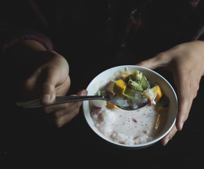 A hand holding a spoon filled with fruit and shaved ice.