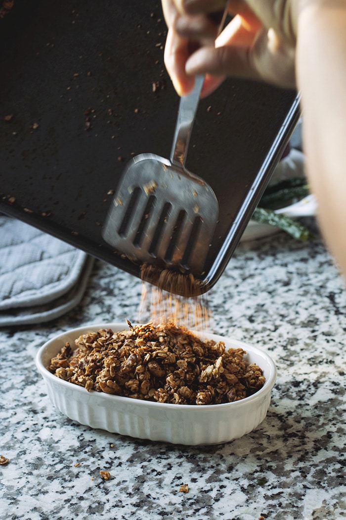 granola pushed off a sheet pan into a white bowl.