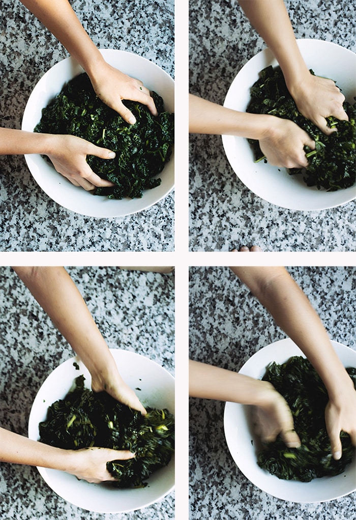 hands massaging kale in a white bowl on a granite countertop.