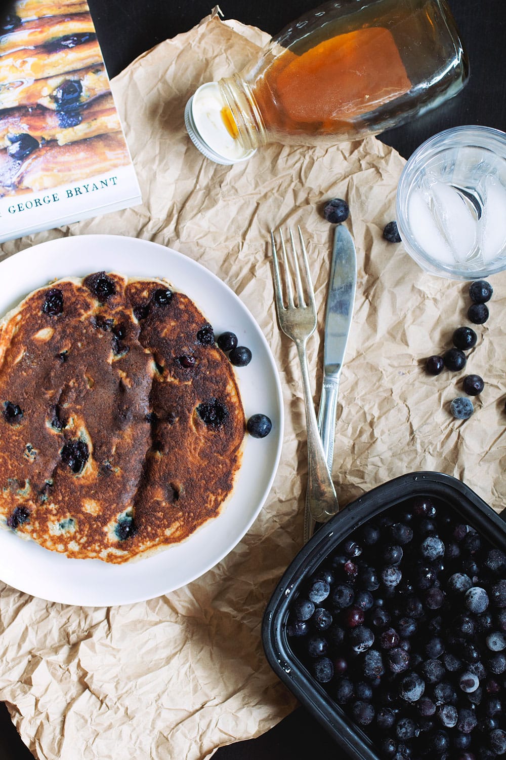 A thick blueberry pancake on a white plate next to a fork and knife.