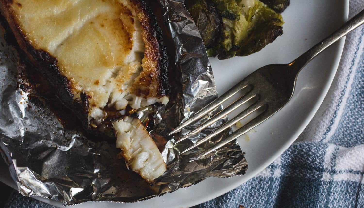 A fork taking a bite of miso-glazed cod on a white plate.