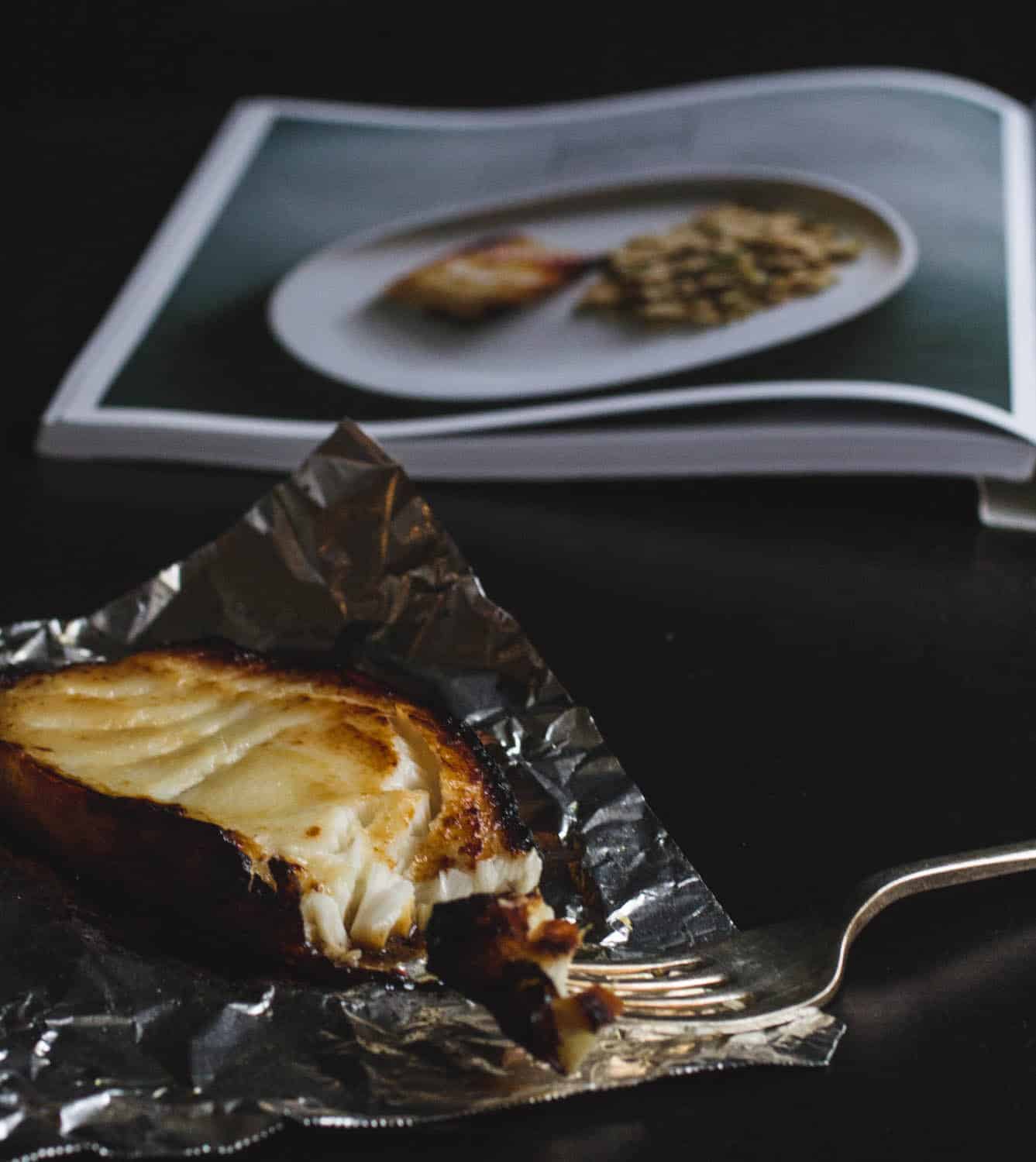A slab of miso-glazed cod on a piece of foil with the Easy Gourmet book in the background.