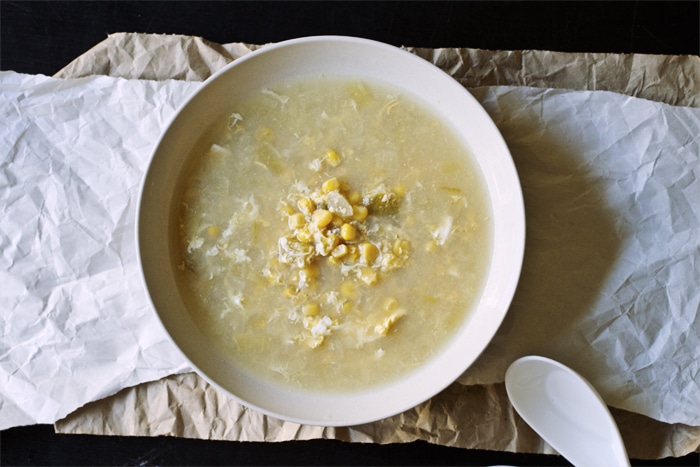 A taupe bowl full of egg drop corn soup on top of a white and brown sheet of paper.