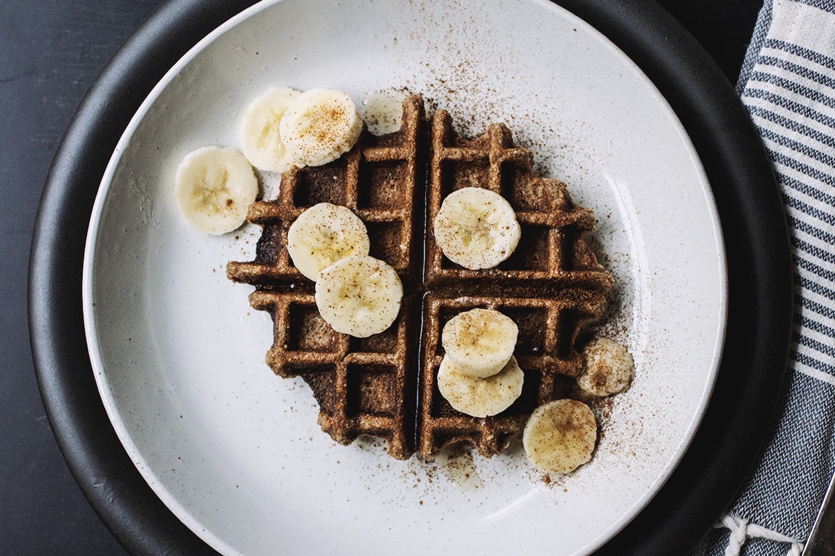 A buckwheat waffle with banana slices on a white plate.