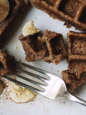 Pieces of a waffle with banana slices and a fork on a white plate.