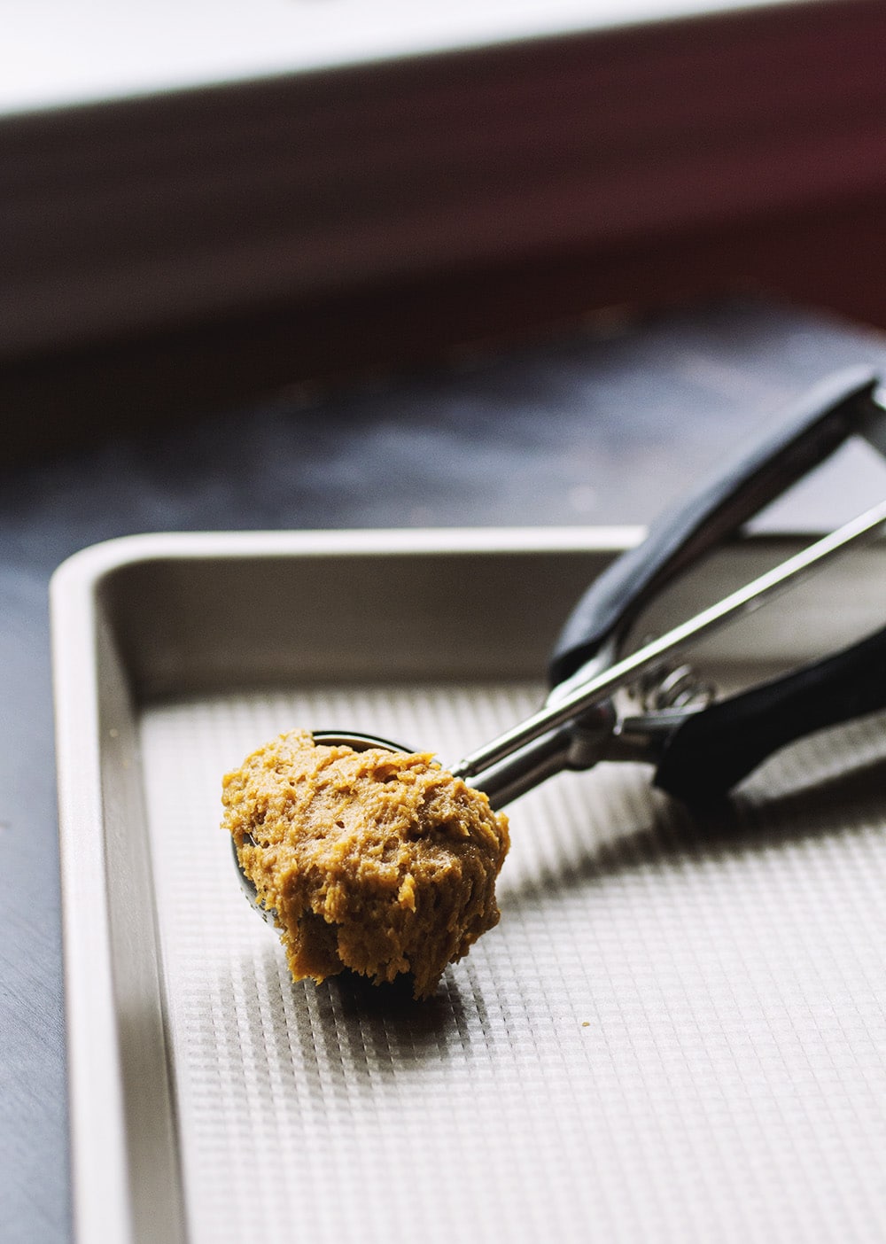 A cookie scoop filled with pumpkin cookie dough resting on a metal cookie sheet.