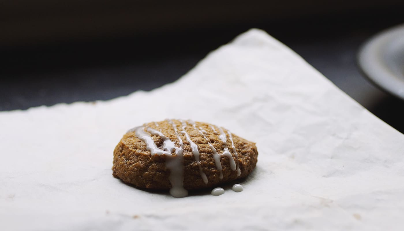 A pumpkin cookie drizzled with white glaze on a piece of white parchment paper.