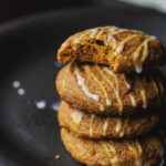 A stack of pumpkin cookies striped with a thin glaze; a bite taken out of the top cookie.