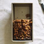 A loaf pan half full of nut-topped banana bread.